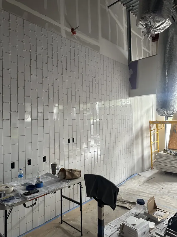 Floor to ceiling white tile wall going up in a retail build out