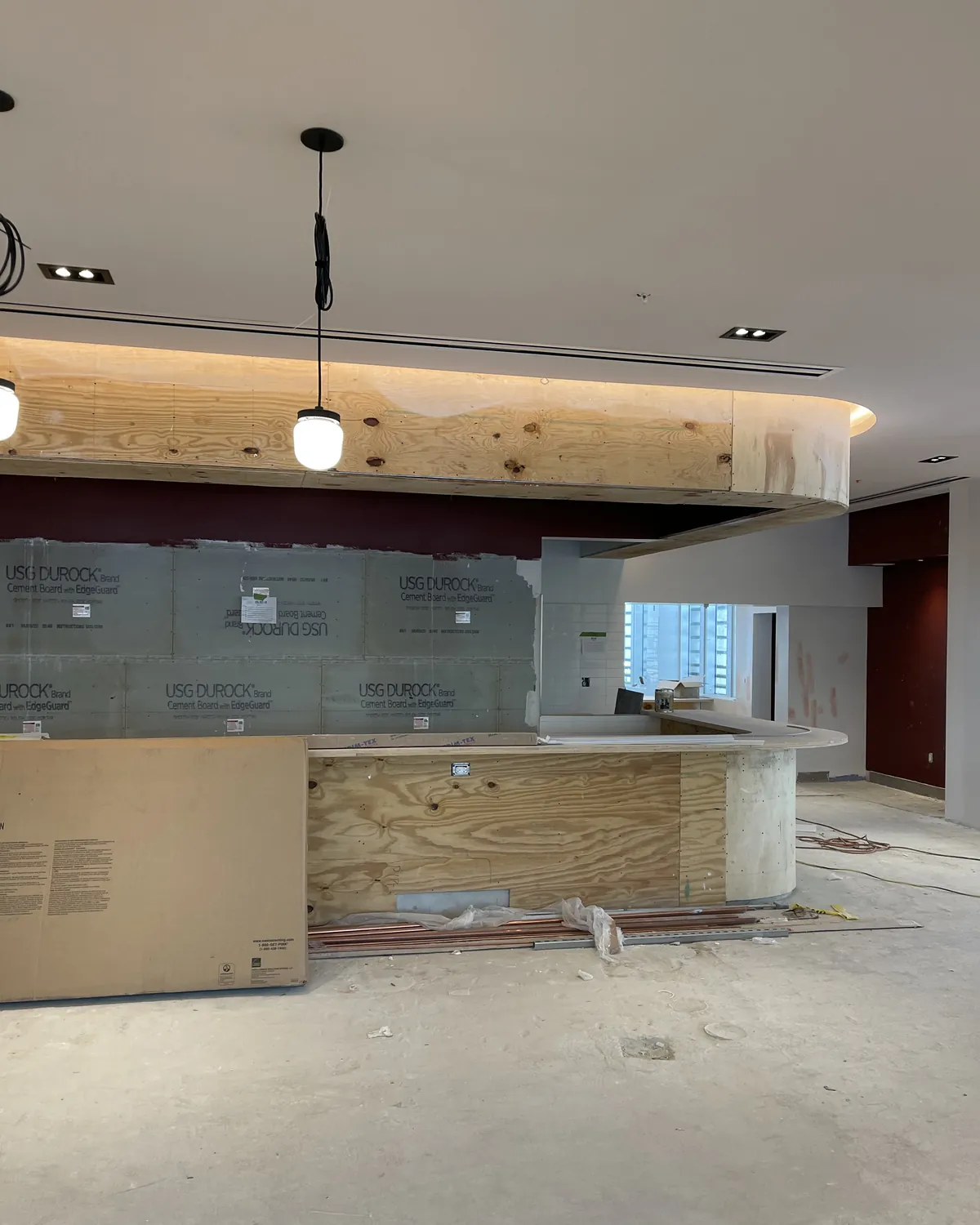 Commercial interior under construction with curved wood soffits, cove lighting and pendant lights in Miami Beach