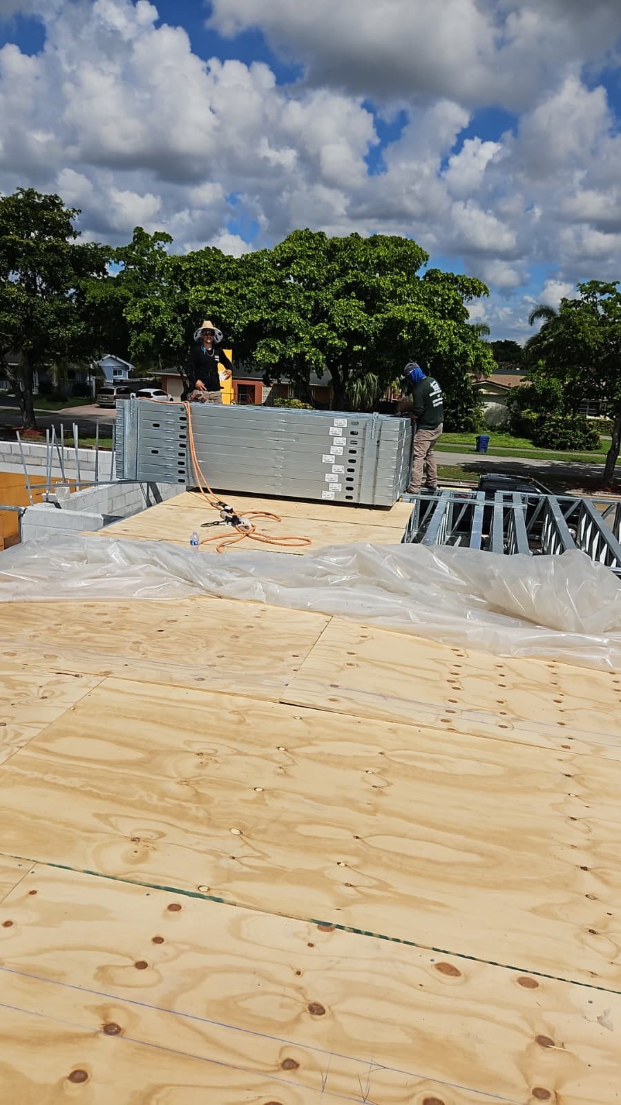 Plywood decking laid over steel framing, with two workers beside a stack of steel framing members.