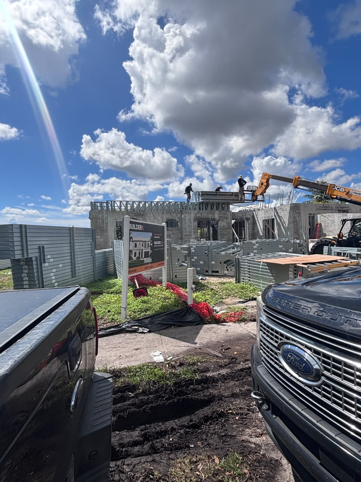 Steel framing panels stacked beside block walls while a telehandler lifts material to workers on top.
