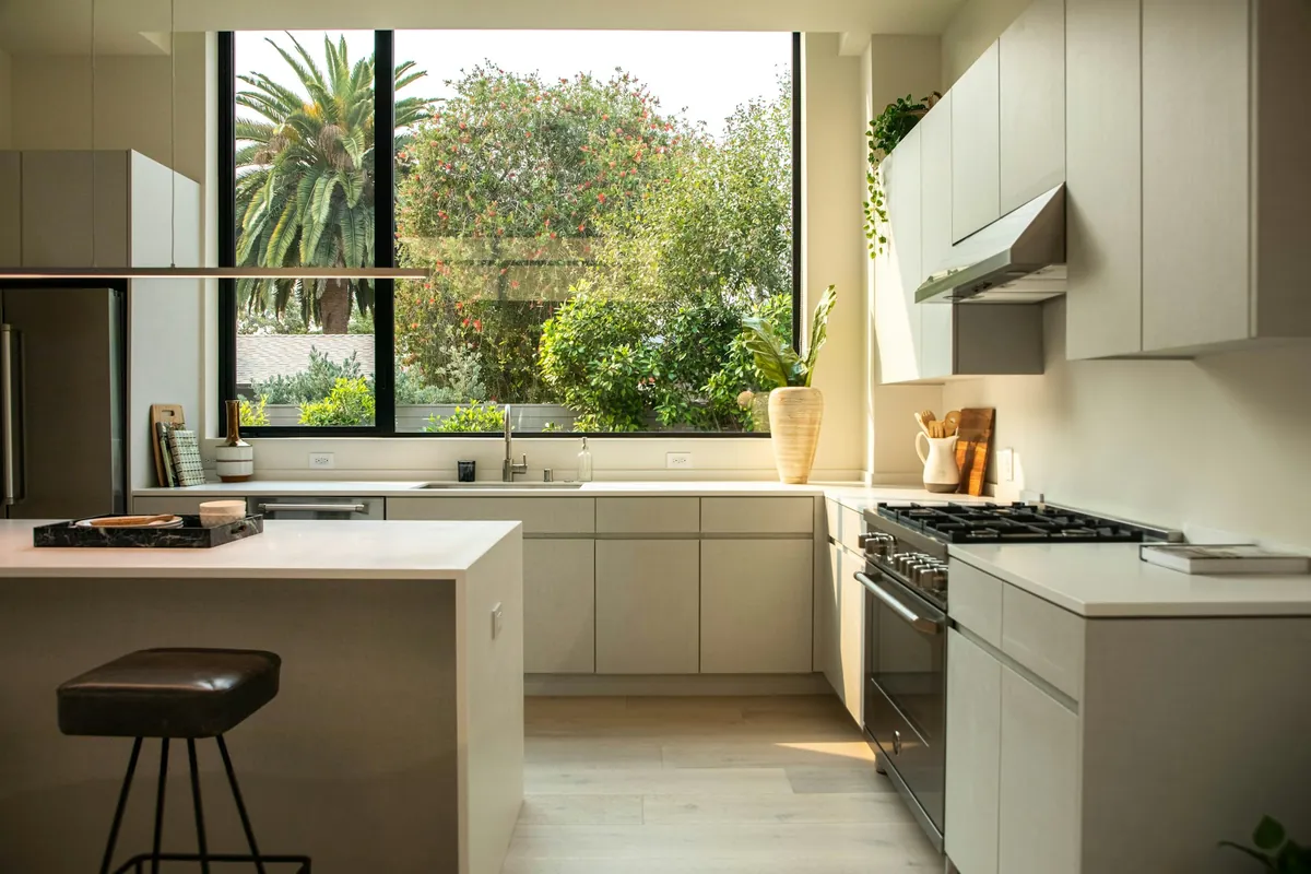 Flat slab cabinet doors with no handles in a sunlit modern kitchen with a large window