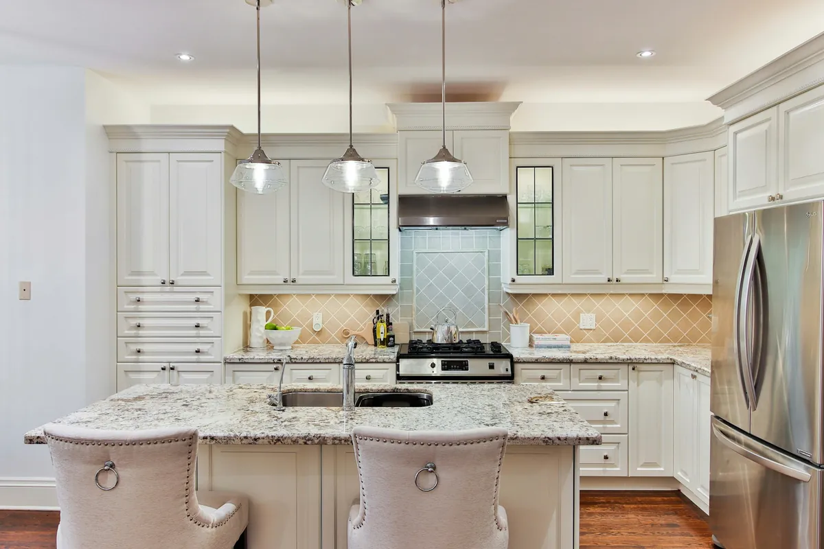 Cream raised panel cabinets around a stone topped island with three glass pendants
