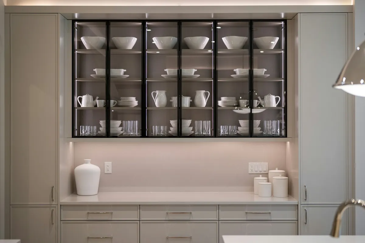 Black framed glass front upper cabinets with lit shelves of white dishes