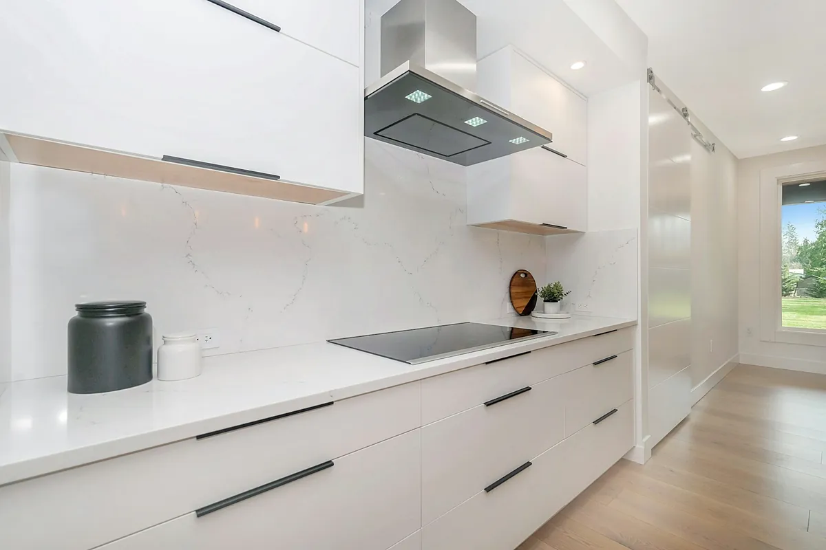 Smooth white gloss slab cabinets with long black pulls and a stainless range hood