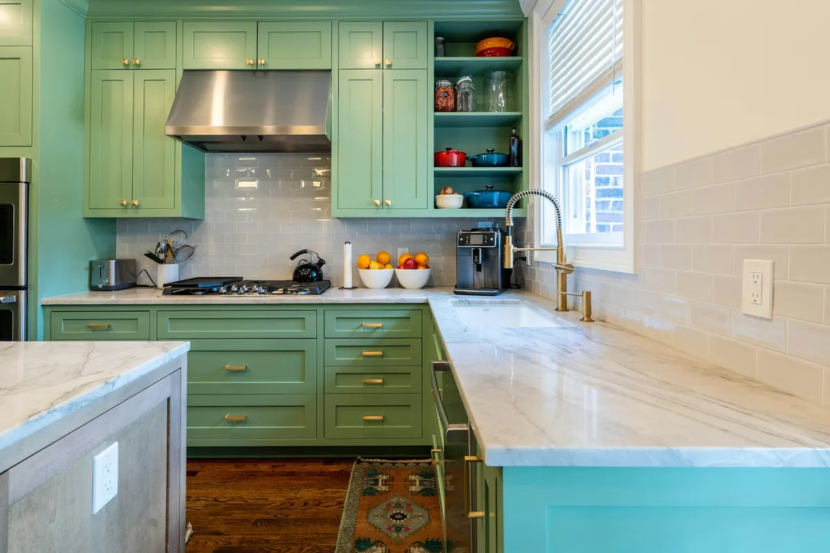 White stone countertops with long gray veins next to green shaker cabinets