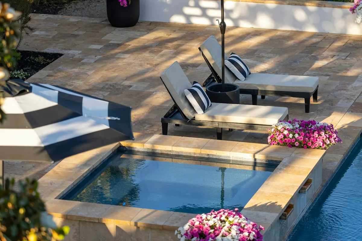 Tumbled stone pavers around a spa and pool with two lounge chairs