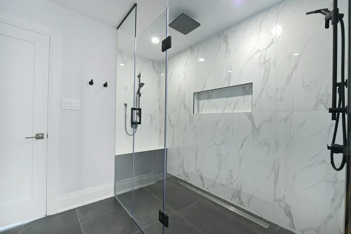 Walk in shower with a frameless glass panel, marble look walls and black fixtures