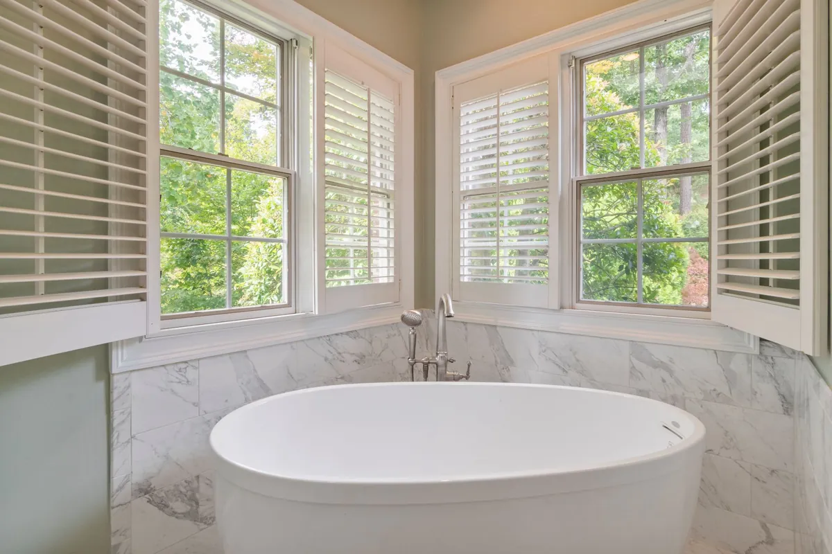 Oval freestanding tub with a floor mounted filler below shuttered windows