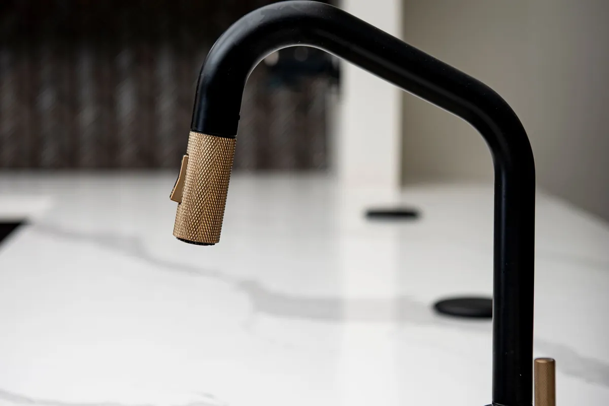 Matte black faucet with a knurled brass spray head over a white stone counter