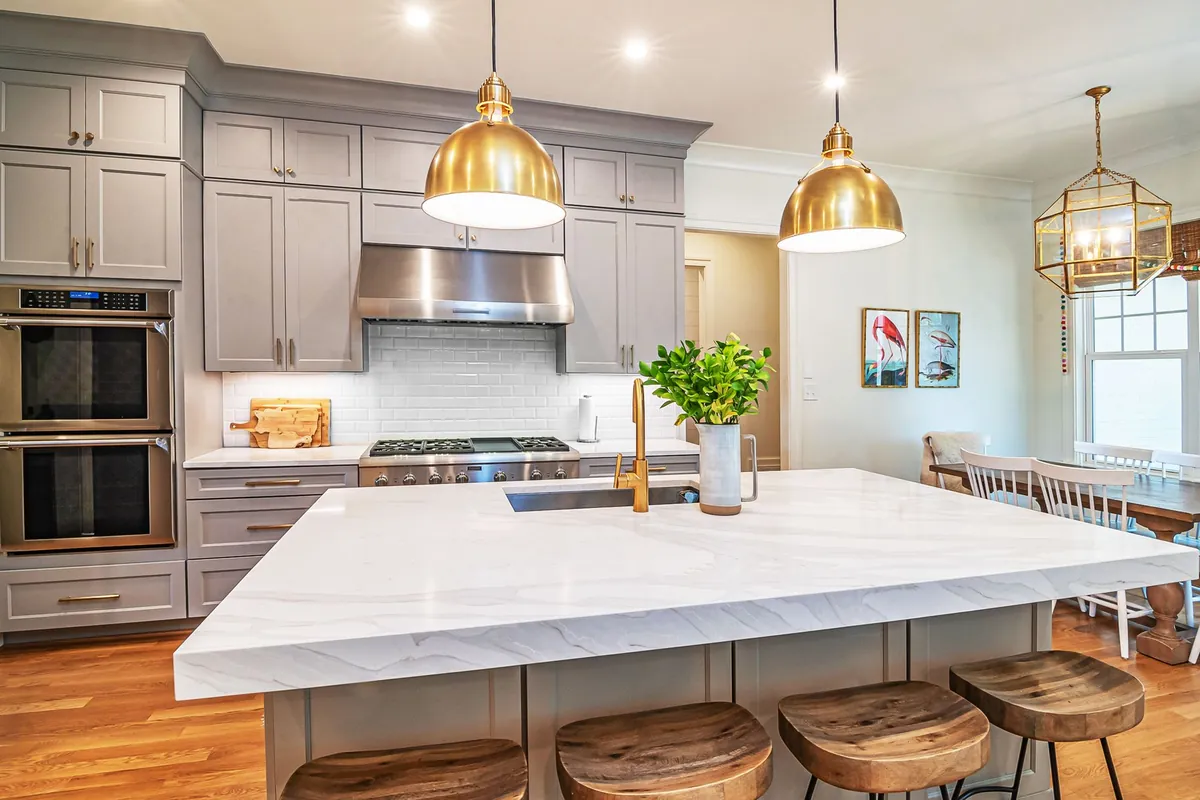 Brass dome pendants over a white kitchen island with a lantern chandelier beyond