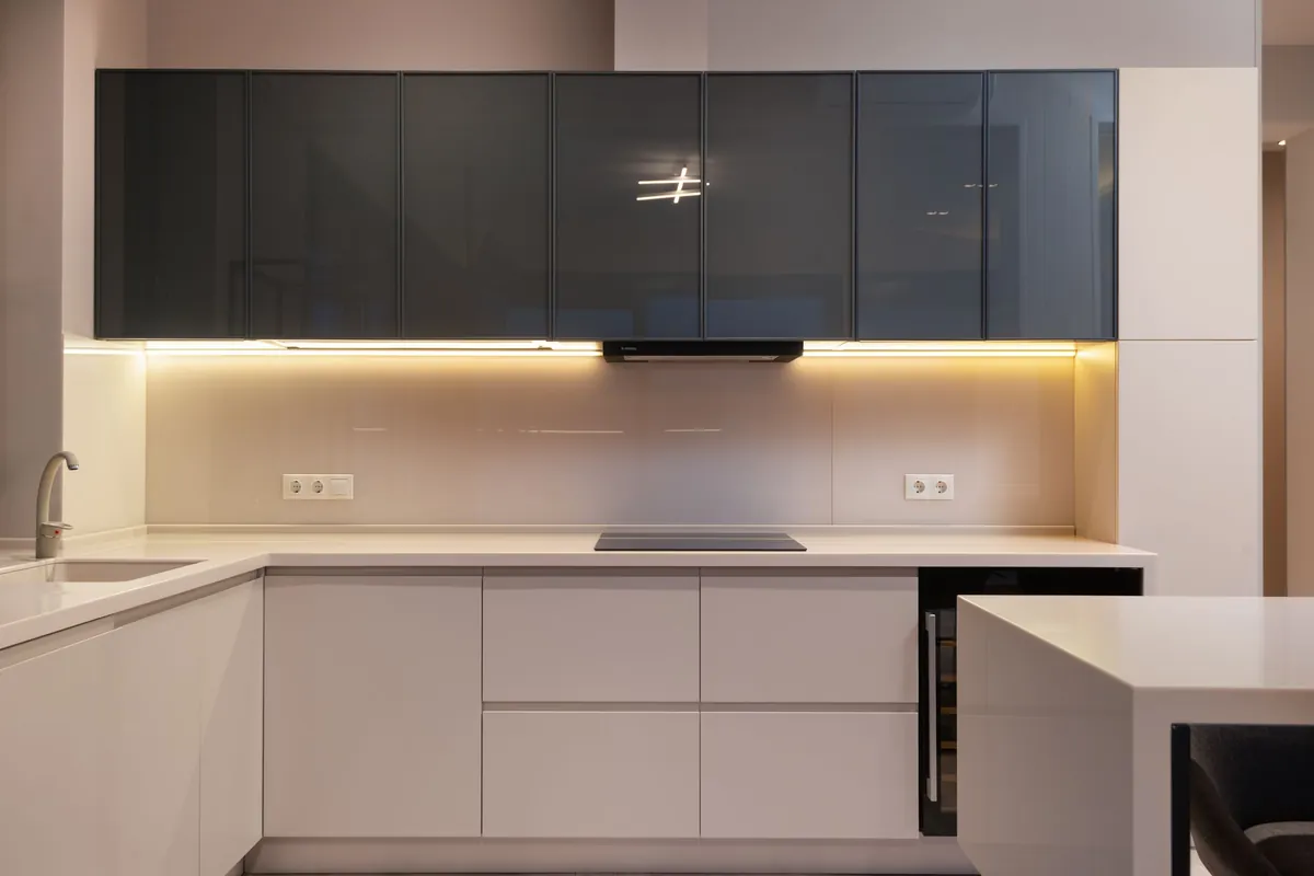Warm LED strip lighting the backsplash under dark glass upper cabinets